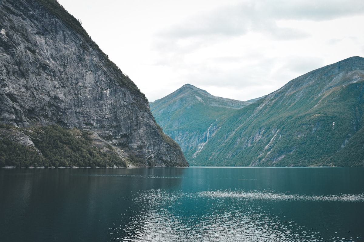 Steep green cliffs flanking a deep blue Norwegian fjord under bright summer skies