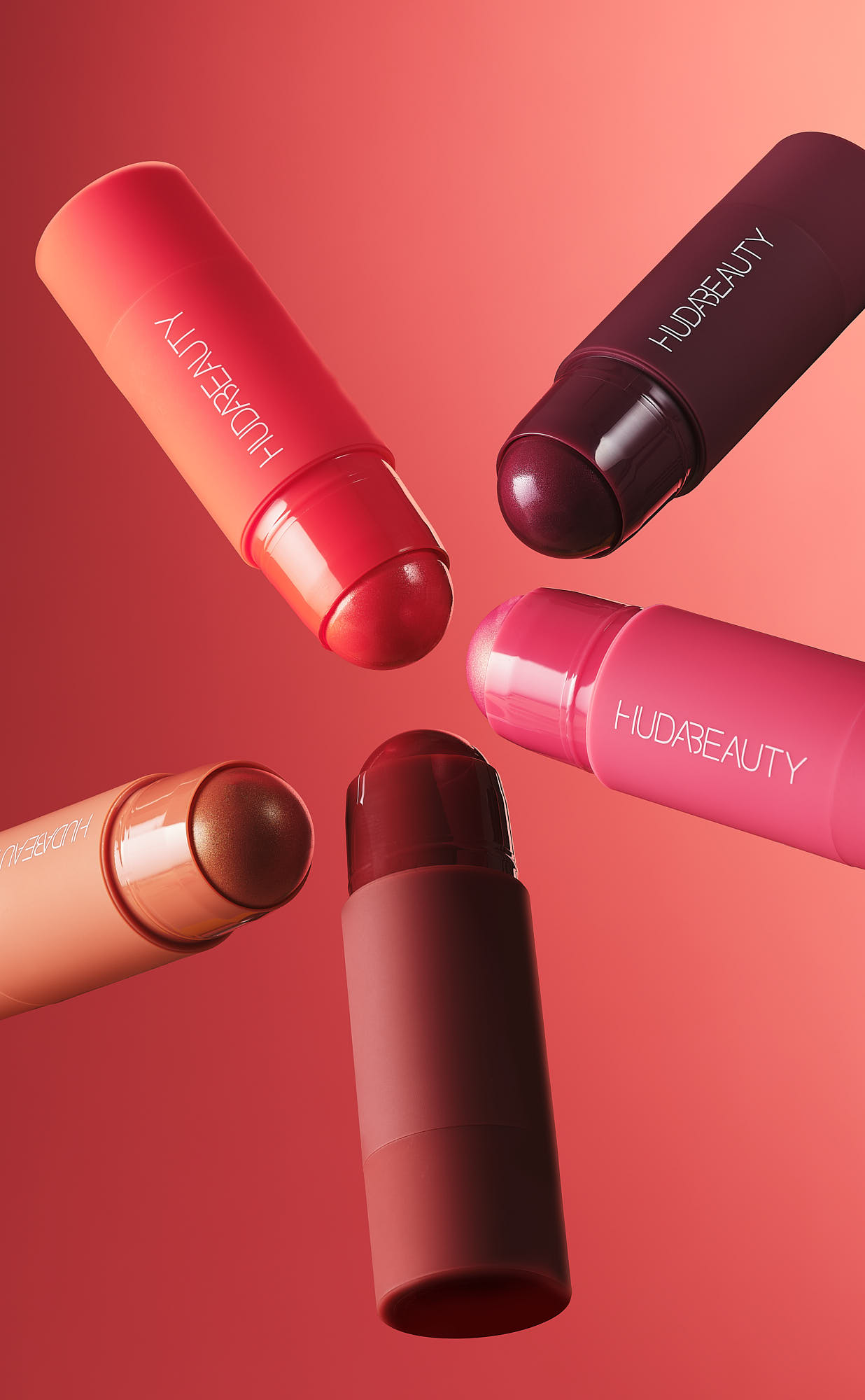Five lipsticks in various shades of red and burgundy arranged against a vibrant red background.