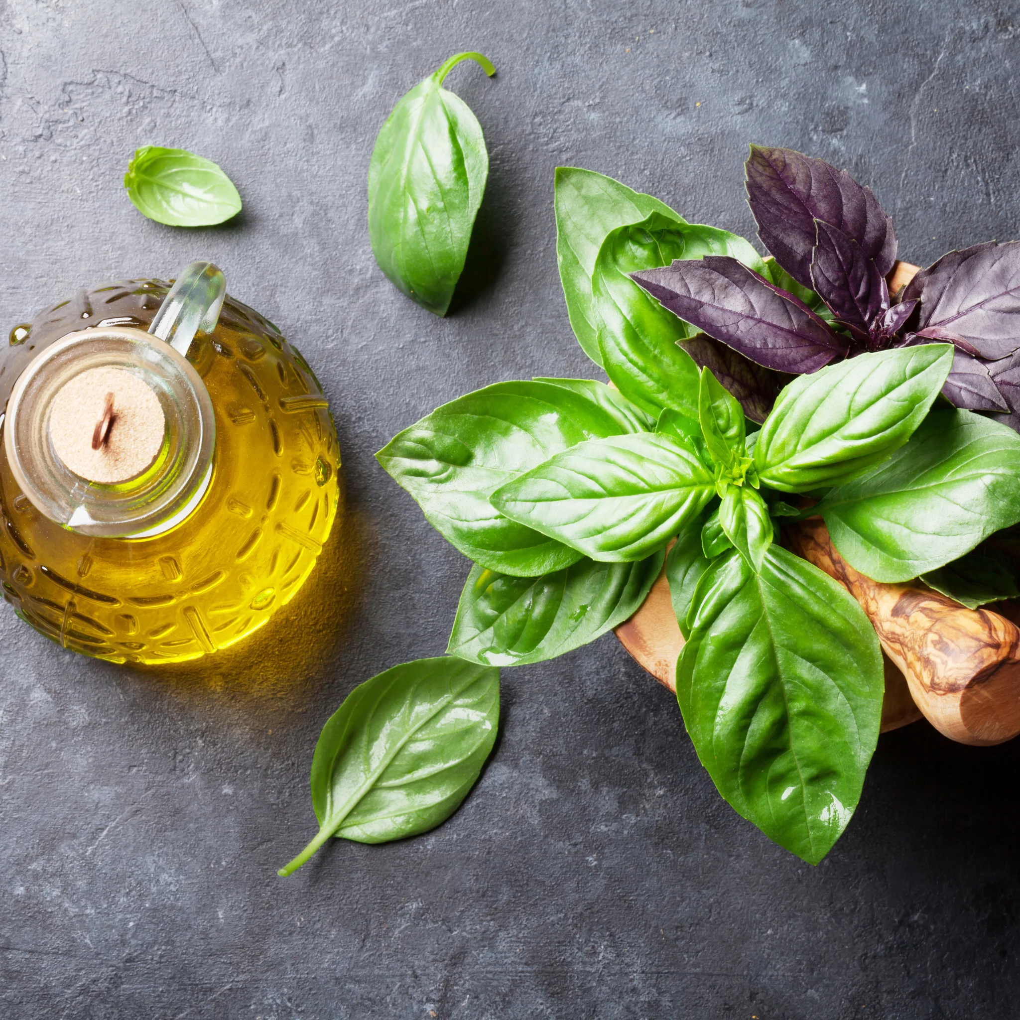 Olive oil and basil on a granite worktop, two essential ingredients in the burrata caprese salad recipe.