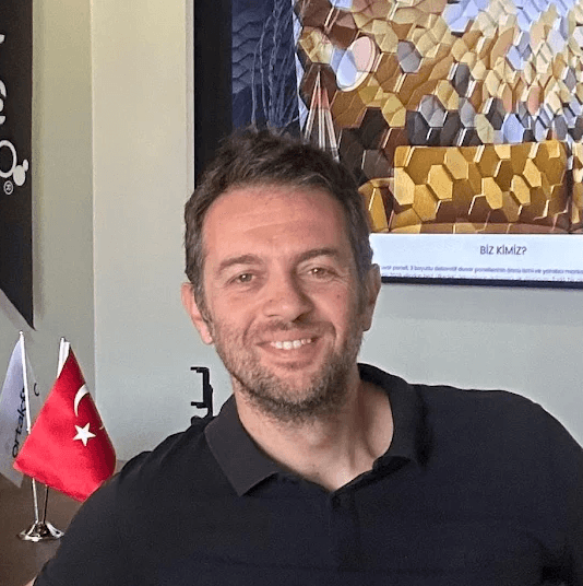 Portrait of a young man with wavy dark hair and a trimmed beard in a white sweater, soft light on a neutral background.