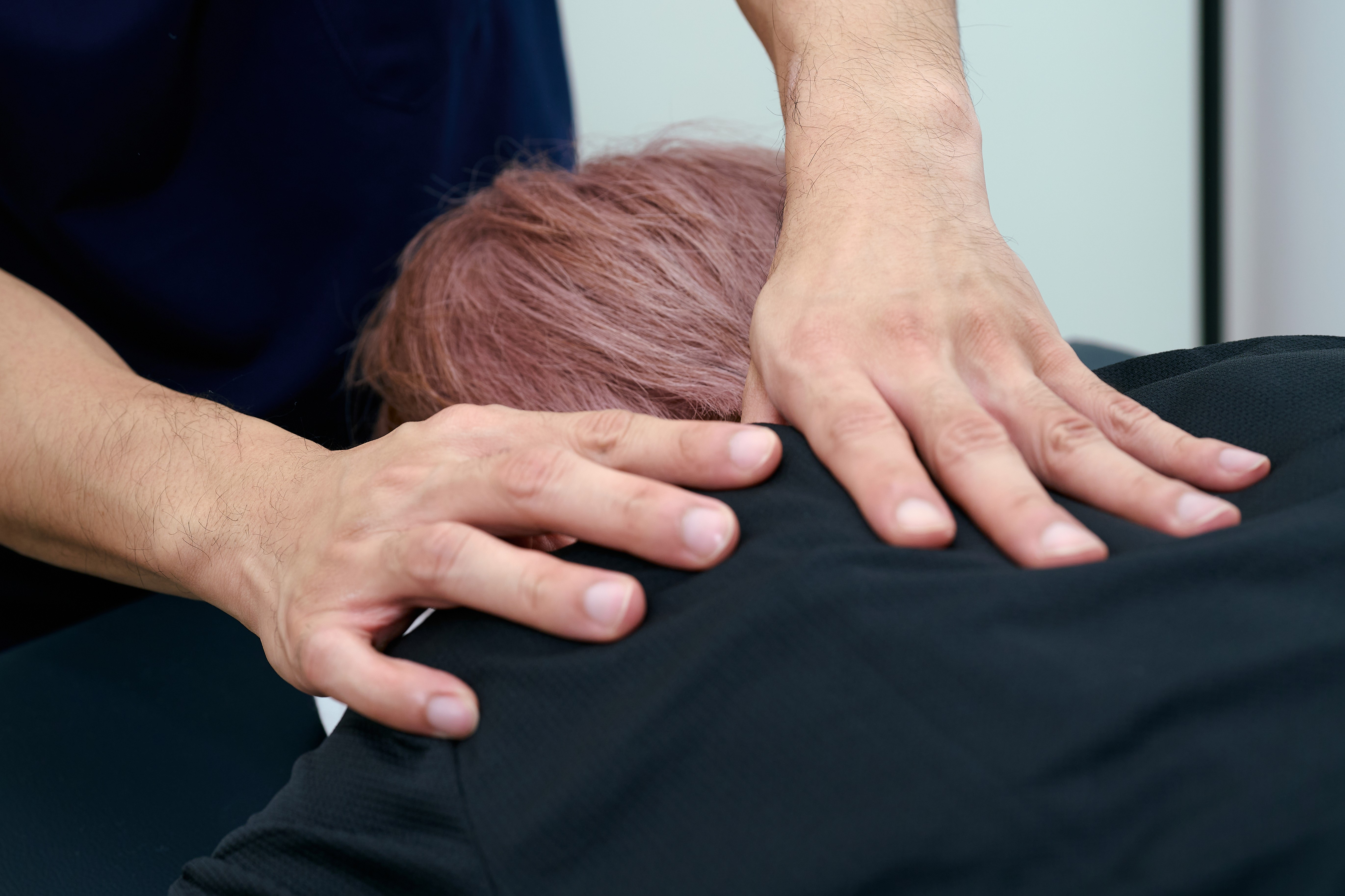A physiotherapist's hands gently massage a person's upper back, demonstrating relaxation and rehabilitation techniques in a clinical setting.