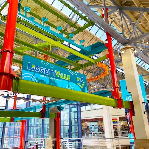 Indoor adventure center with colorful rope courses, featuring green, red, and blue structures, and a "LiGGEtTViLLE Adventure Center" sign.