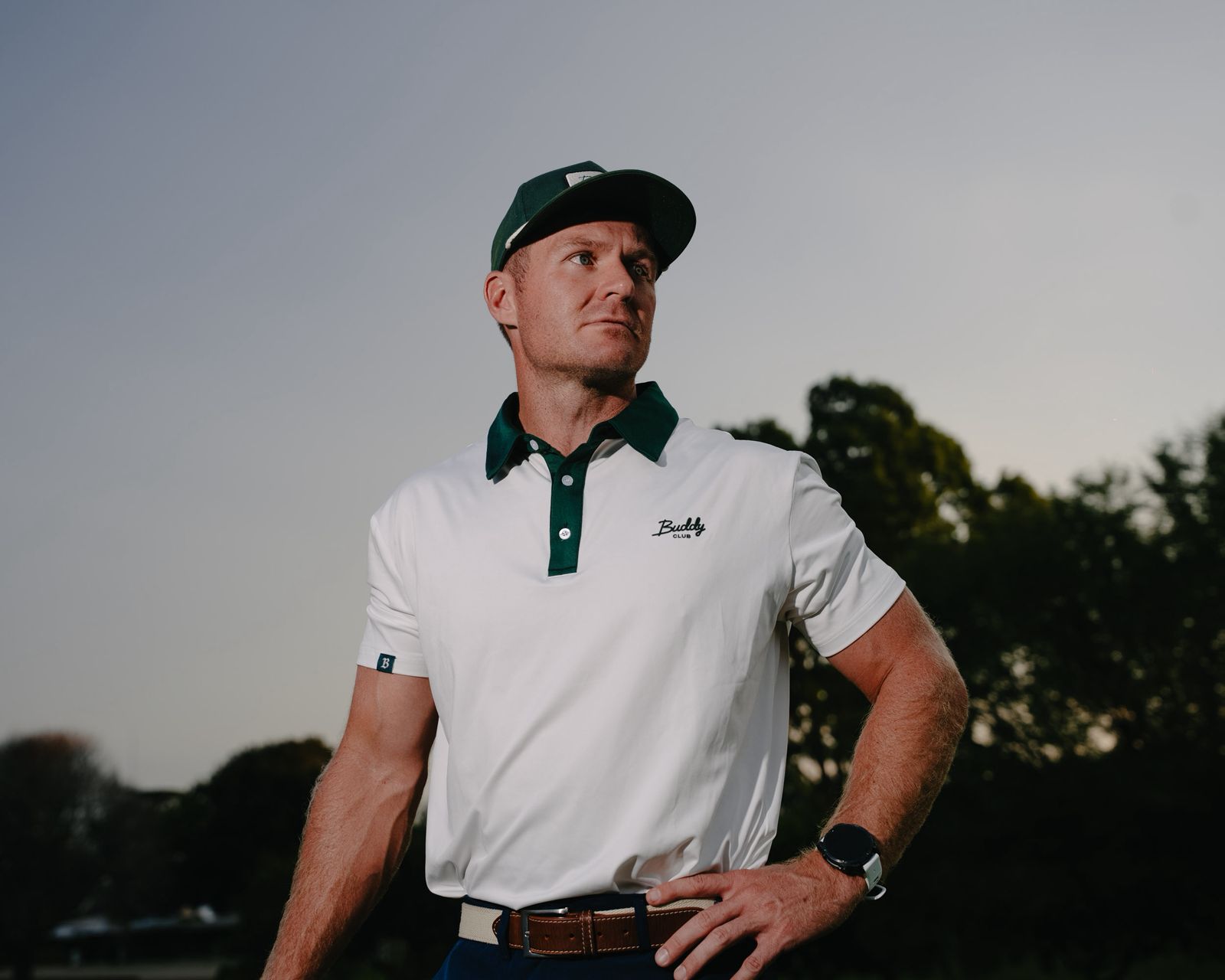 Man dressed in dark casual wear sitting alone in a stadium’s empty rows of purple chairs, lit by dramatic moody lighting.