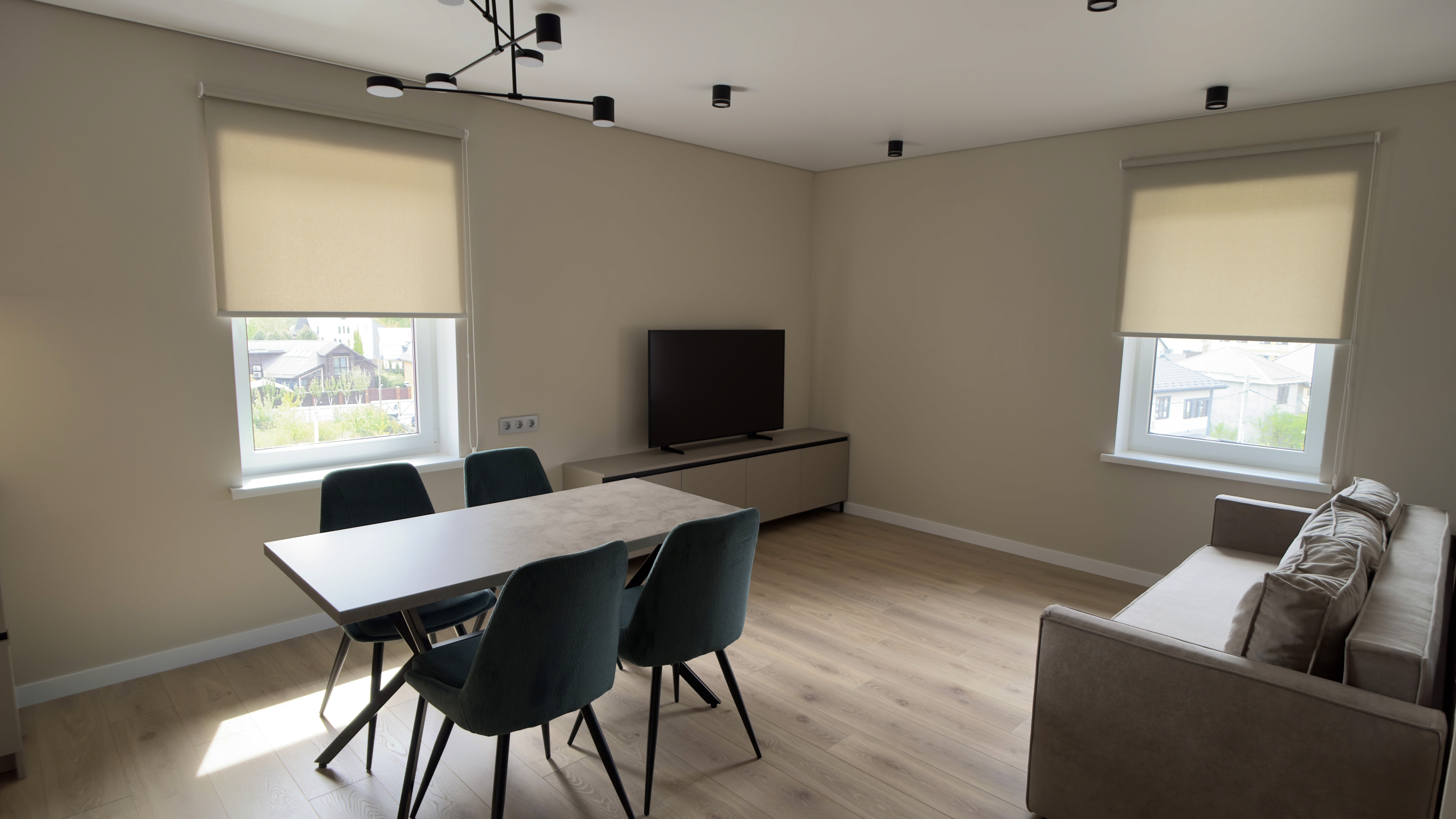 Кутова зона вітальні з телевізором, двома вікнами та обіднім столом