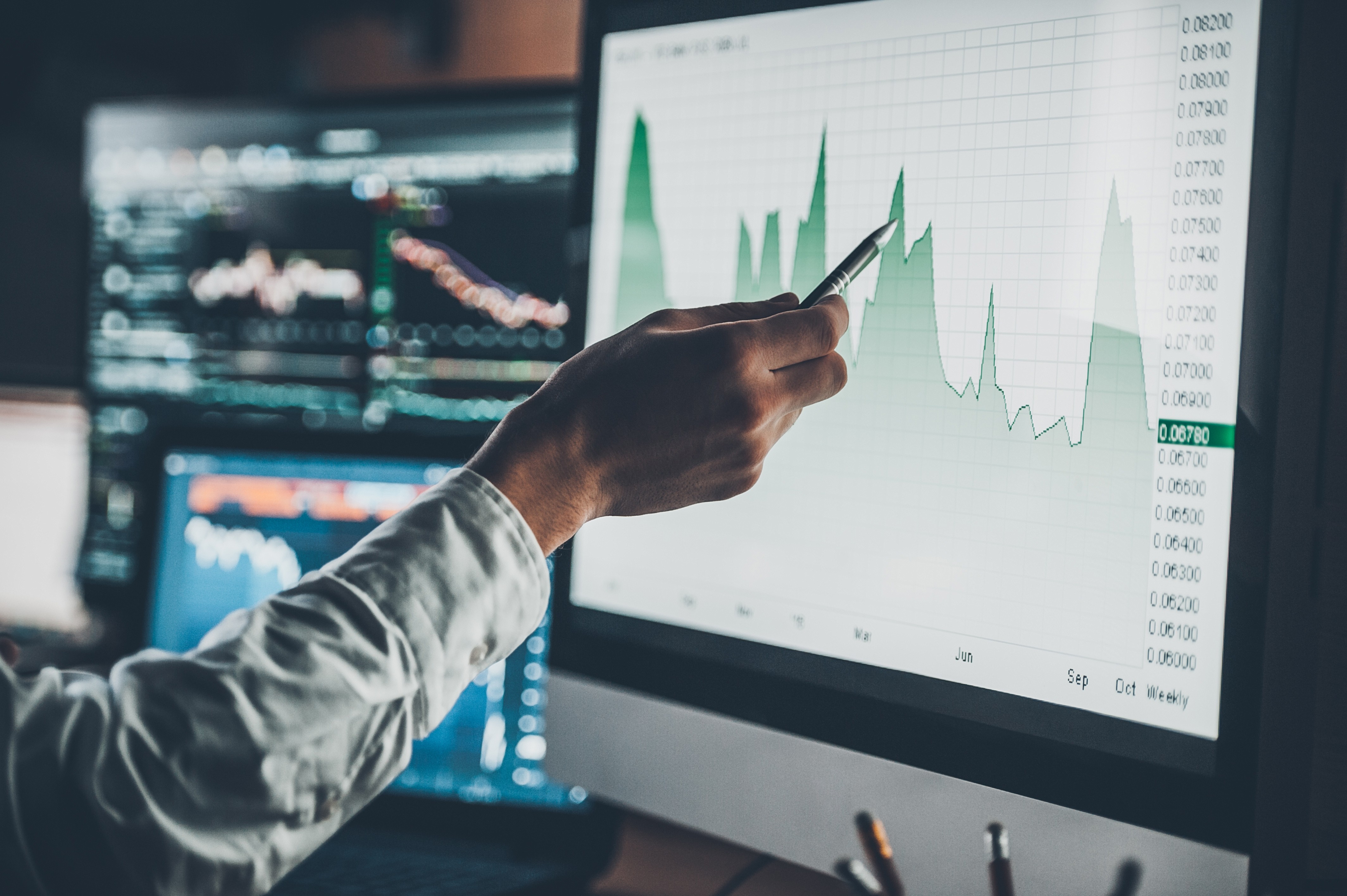A hand holding a pen pointing to a graph on a screen.