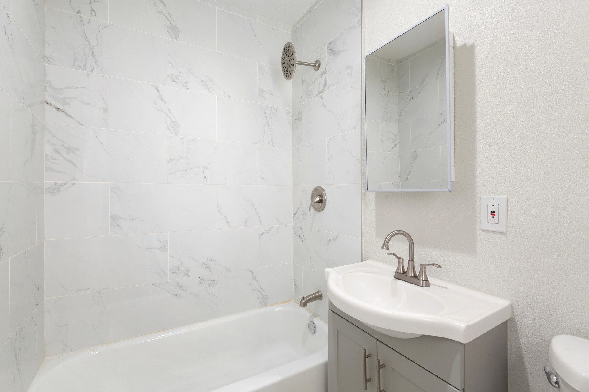 A clean, modern bathroom at 4421 wall, with a white bathtub, shower, and a small sink with a mirror above it.