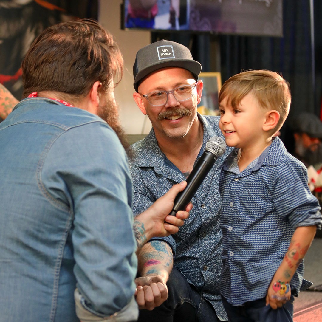 Chris Trew and Jesse Smith holding a microphone listening to a child on stage at the richmond tattoo and arts competition