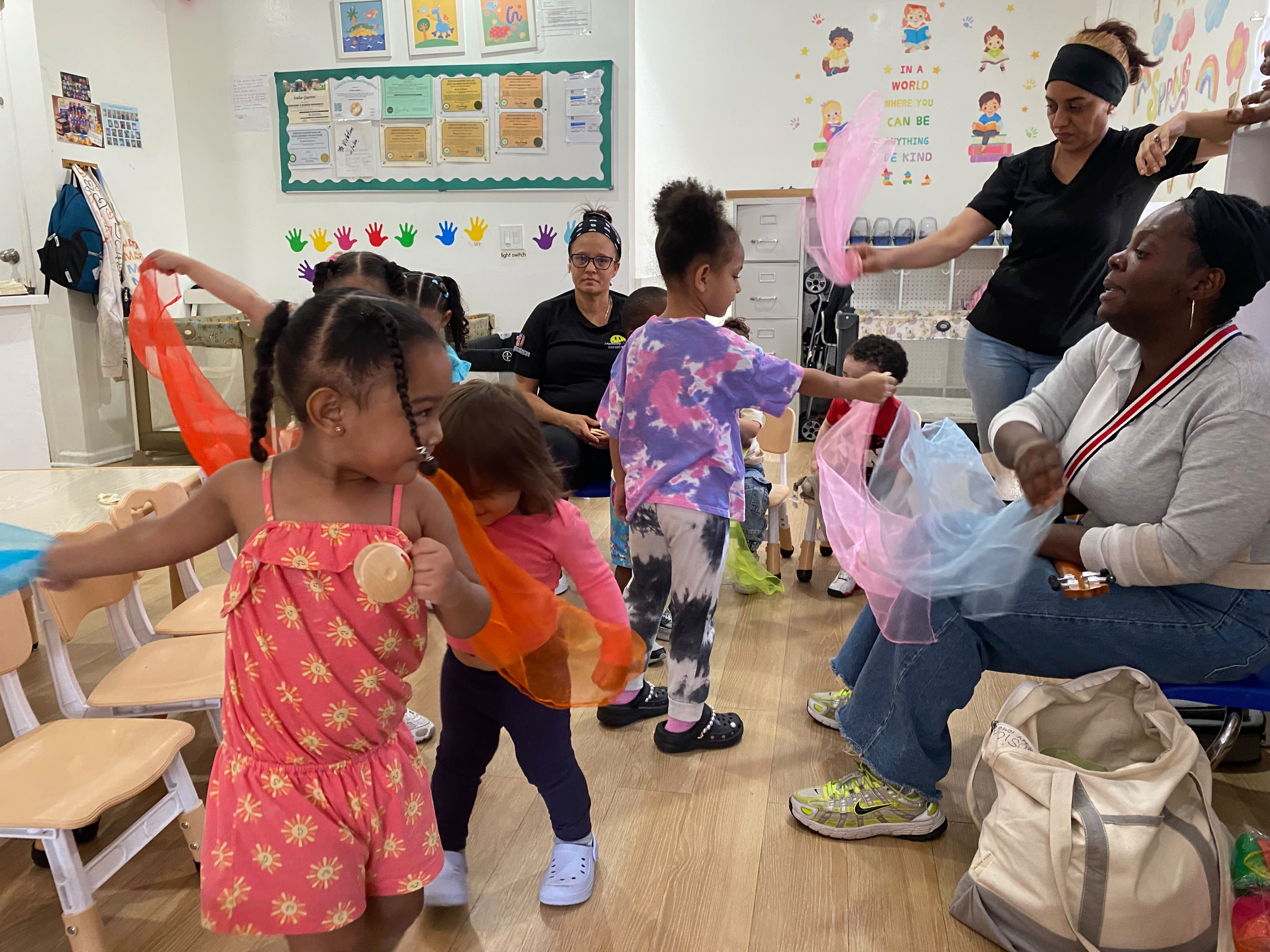 Music teachers guide preschoolers along in a musicla dance while waving gauzy pieces of fabric.