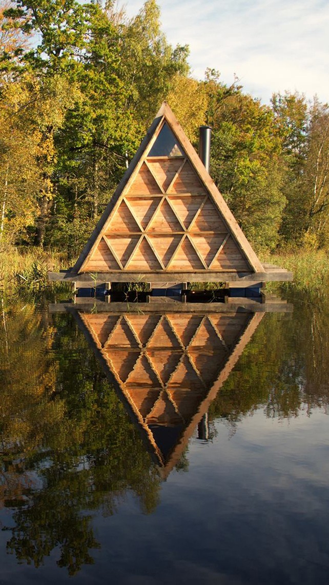 Floating Sauna with triangular timber facade reflected in forest lake designed by Asger Risborg Jakobsen