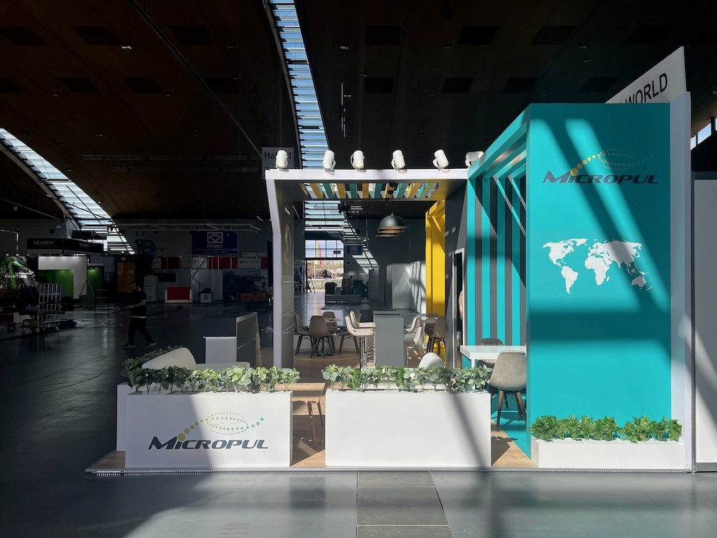 Alternate view of the Micropul stand showing wooden flooring, greenery, and the energetic brand environment.