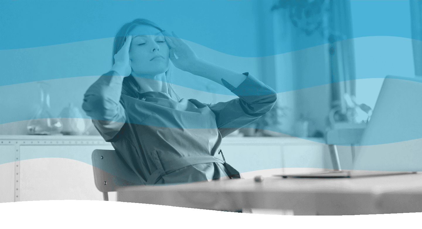 A person sits at a desk in an office setting, looking relaxed with arms raised and eyes closed, suggesting a moment of stress relief.