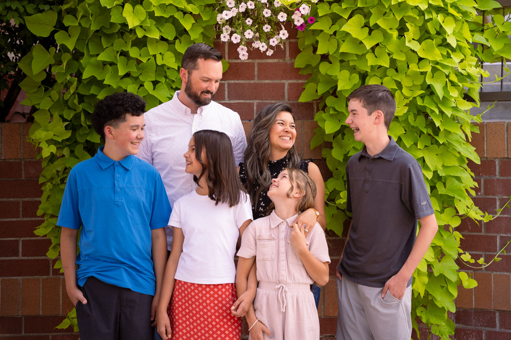  a beautiful family with a brick wall behind them and green foliage draping over the brick wall