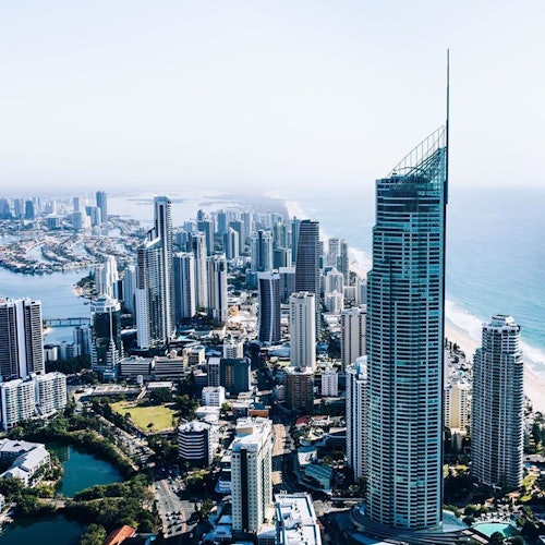 Aerial view of a coastal cityscape with numerous high-rise buildings along a beach and a large, distinct skyscraper in the foreground.