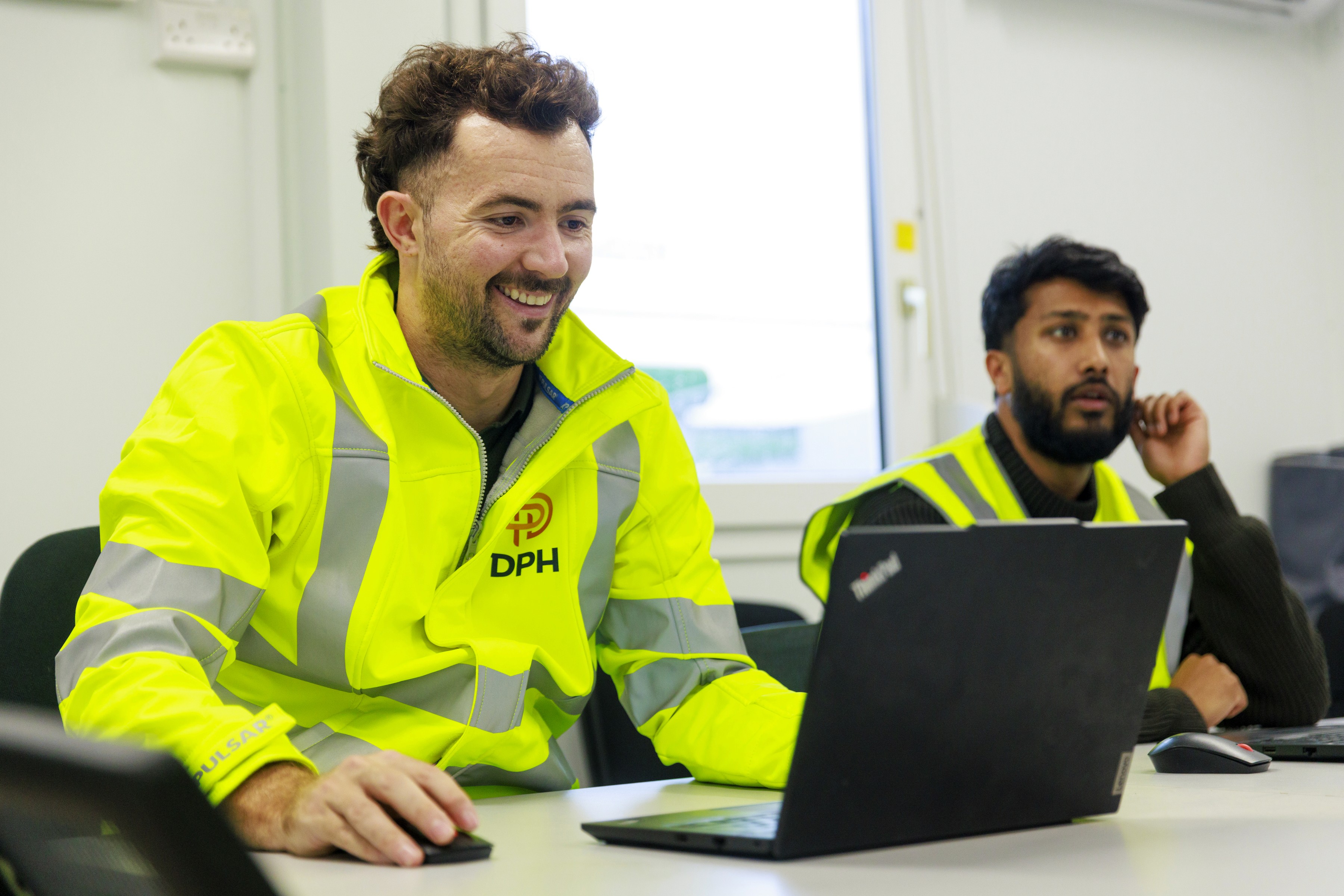 Modern glass building with illuminated interior and reflections at sunset