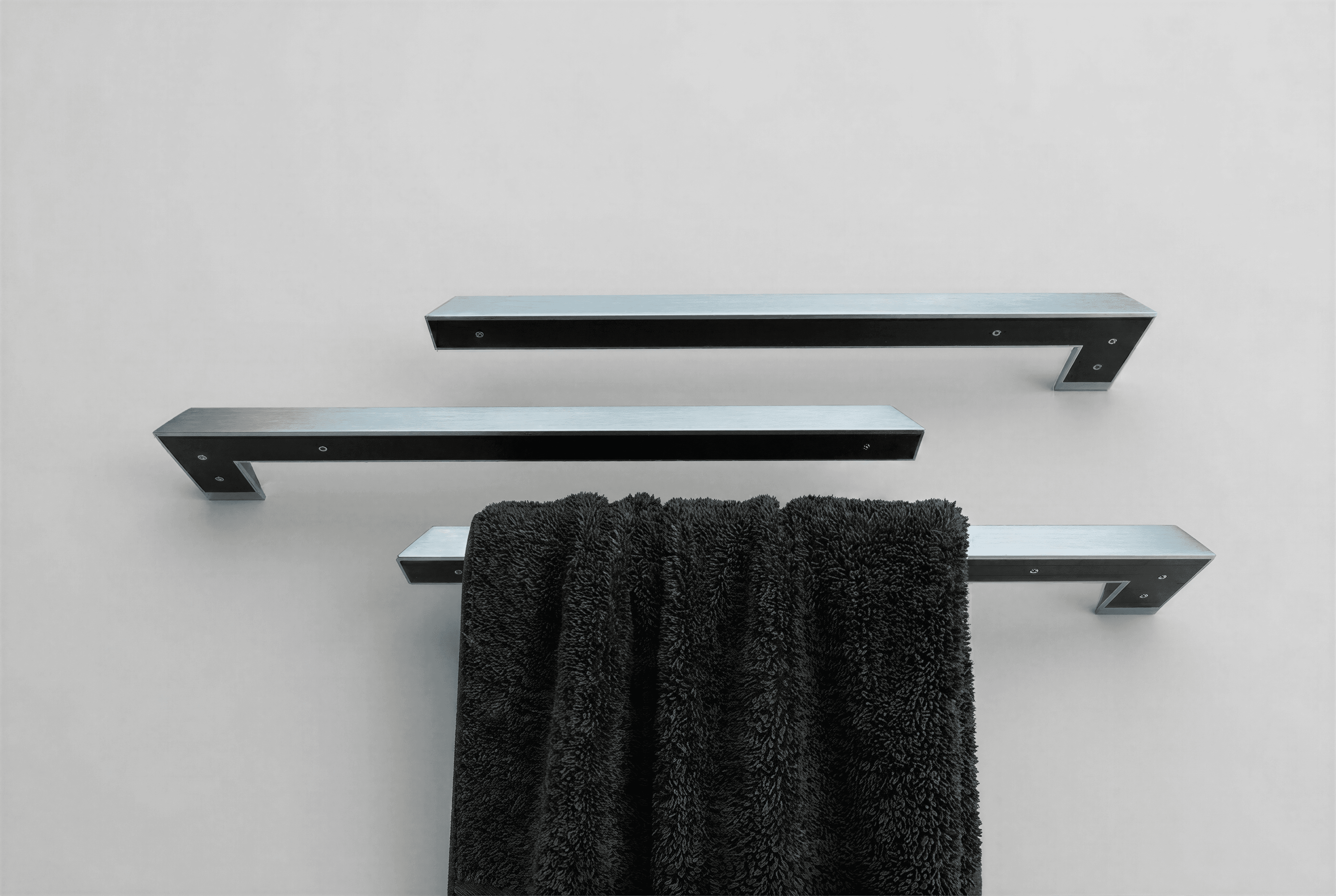 Three towel holders mounted above each other on different sides, with the lowest holding a black towel, mounted on a white wall.