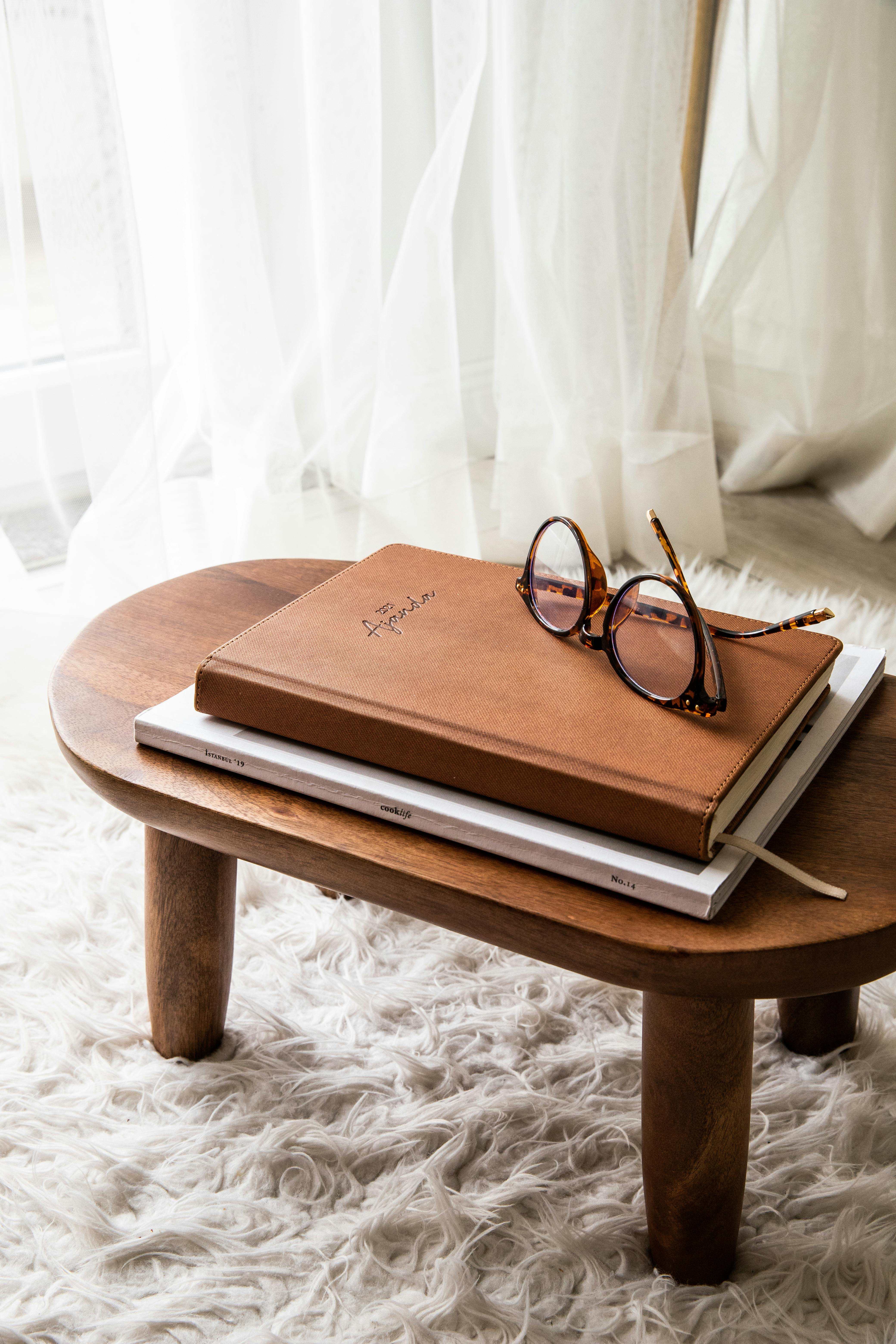 Books and glasses on a coffee table, with the table placed on a white, high-pile rug, and a white curtain in the background.