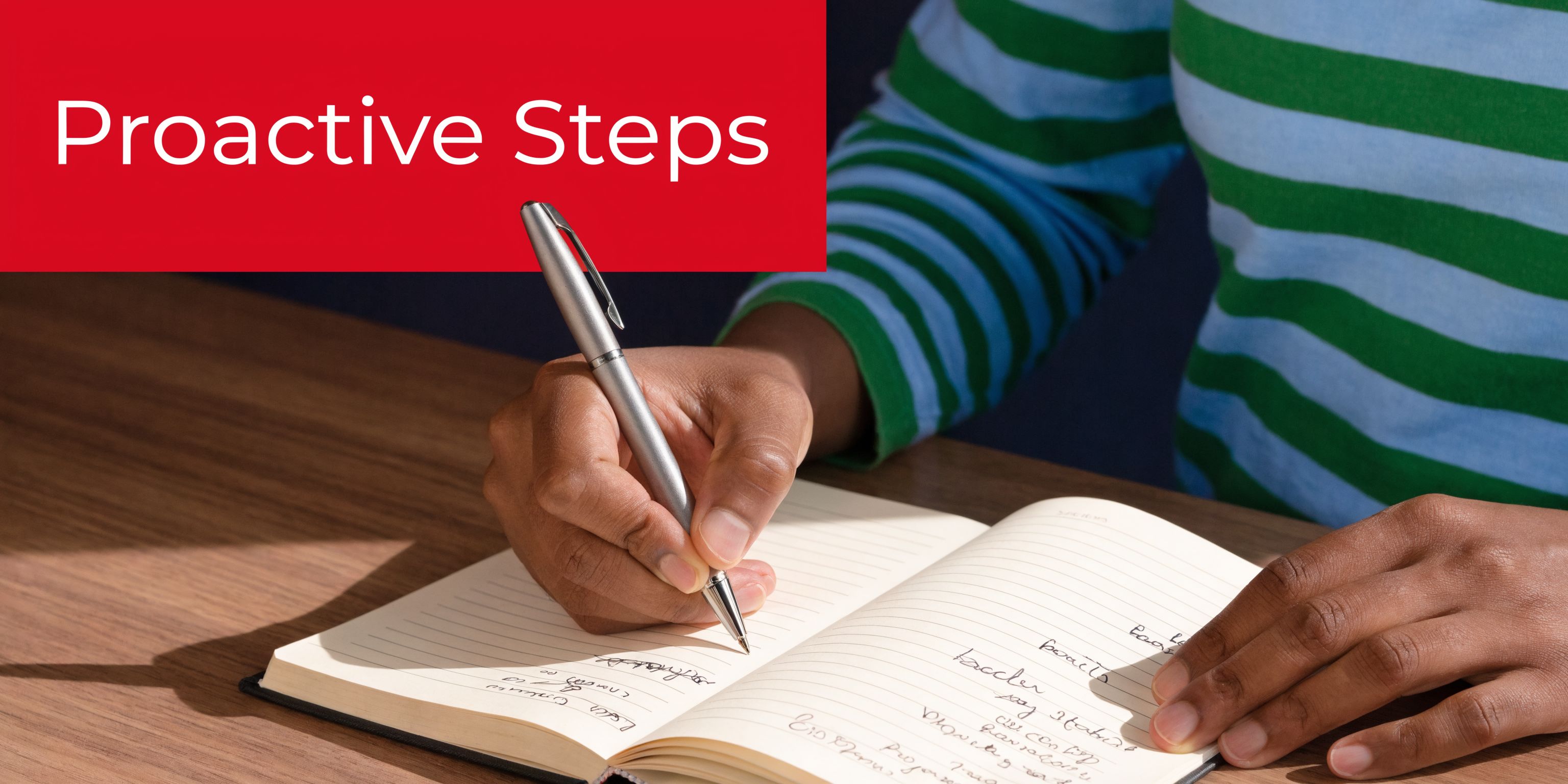 A person wearing a striped shirt writing proactive steps in a notebook at a wooden table.