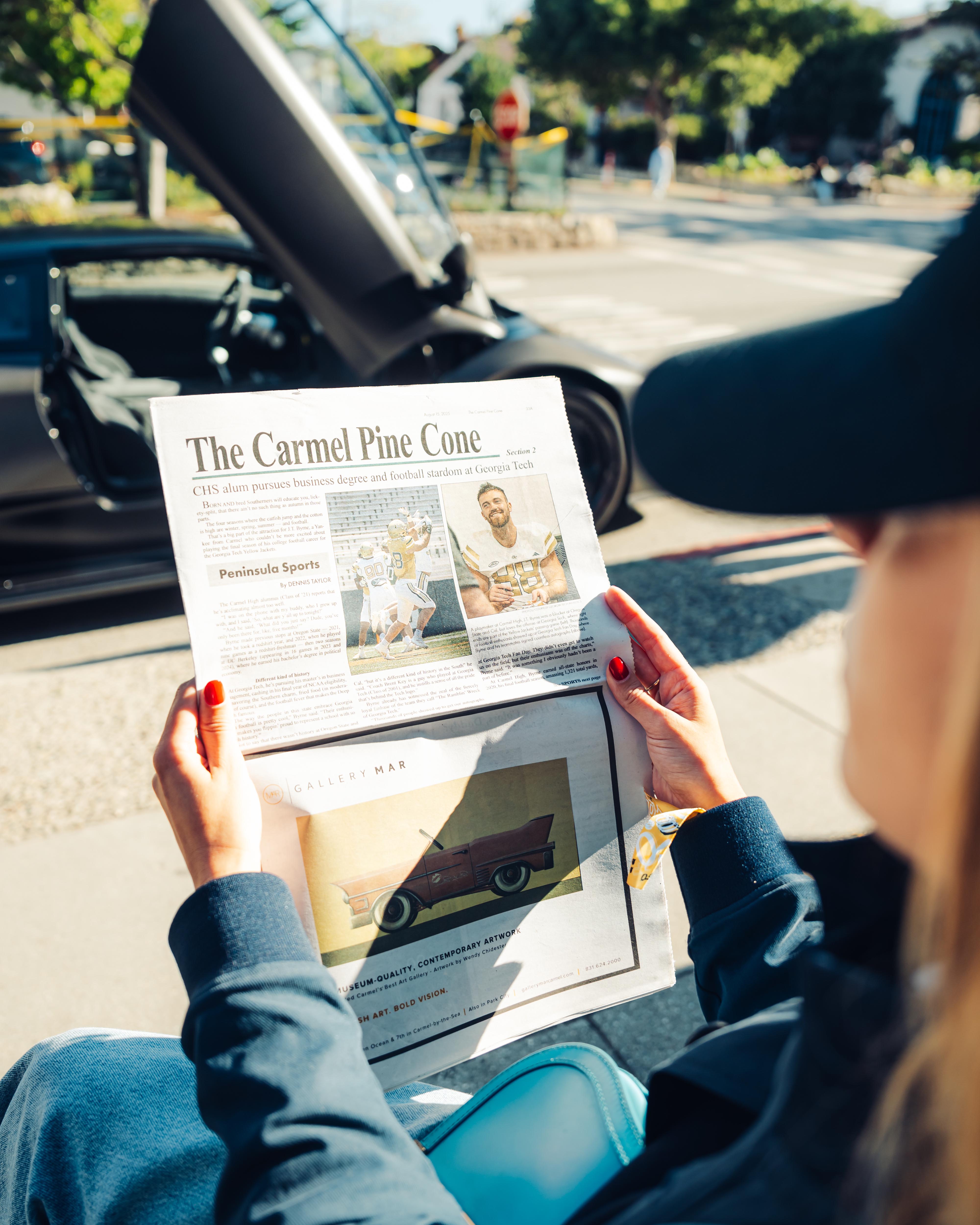 Persona legge giornale con auto sportive sullo sfondo