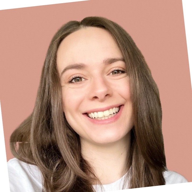 Lächelnde Person mit langen braunen Haaren, die ein weißes Oberteil trägt, vor einem sanften rosa Hintergrund.