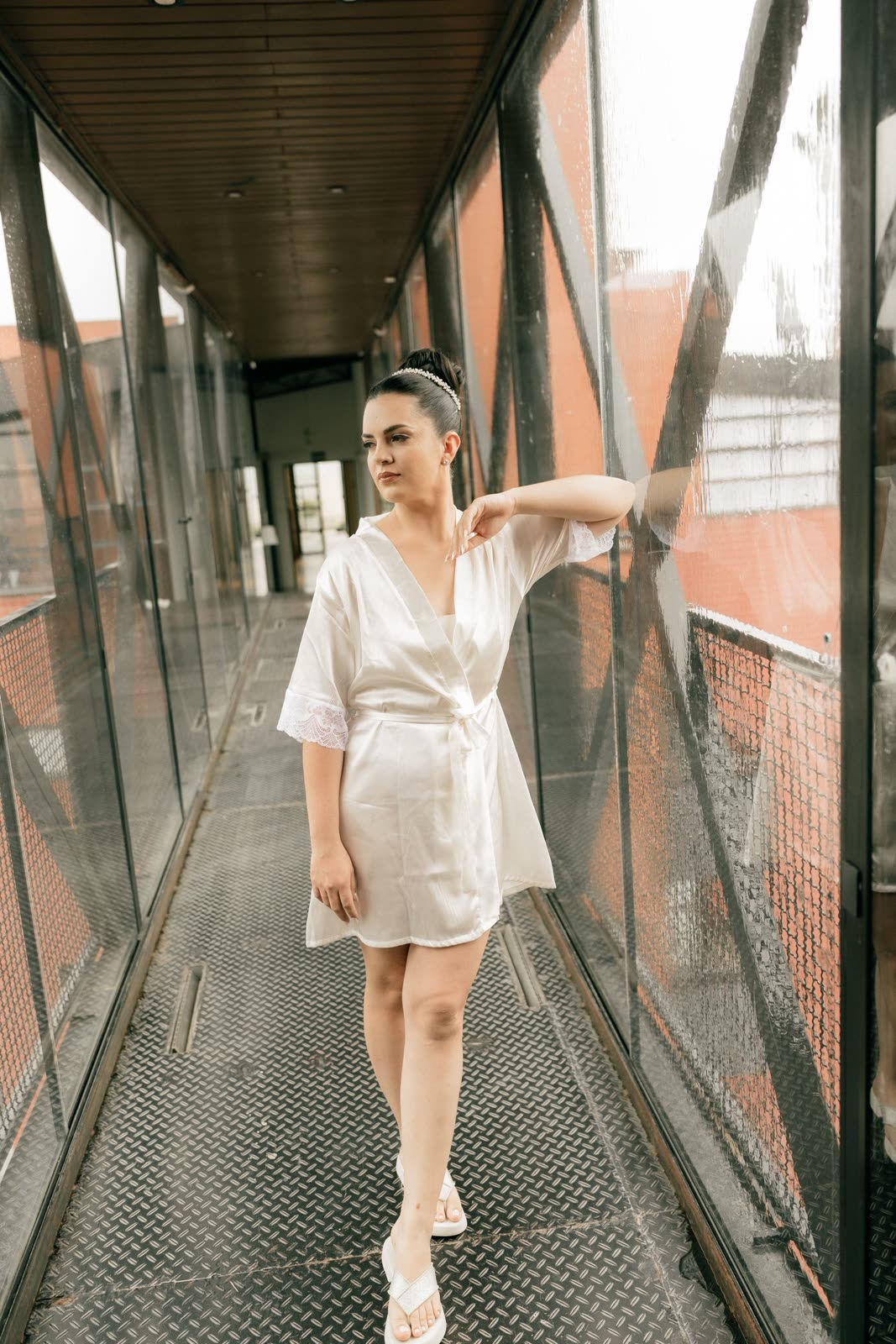 Bride in a white satin robe leaning on a glass and steel walkway