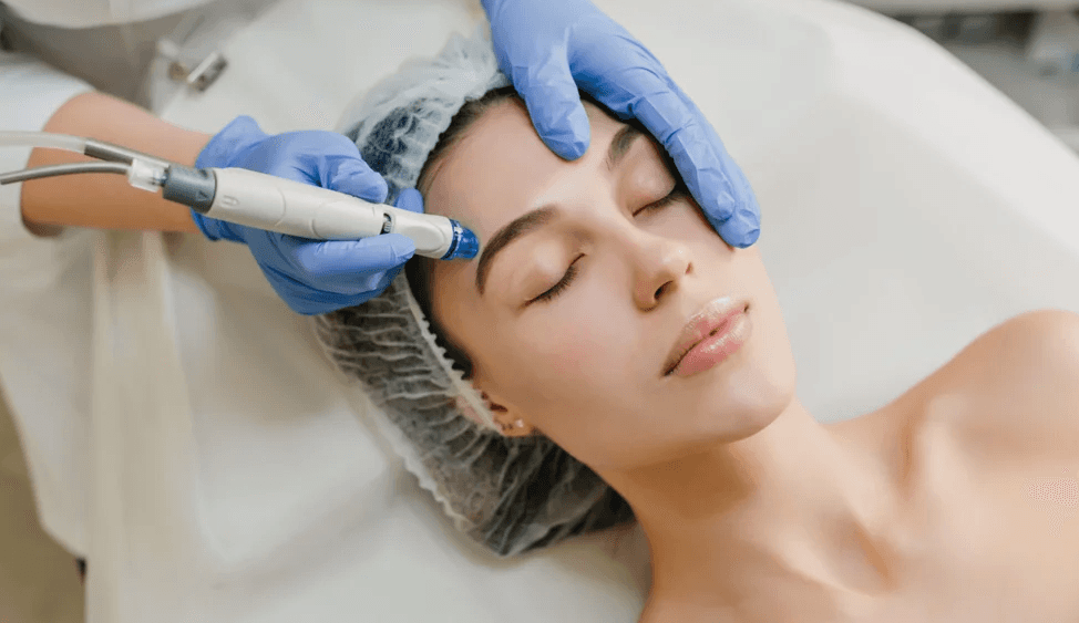 Aesthetician using Hydrafacial machine tip on woman's forehead.