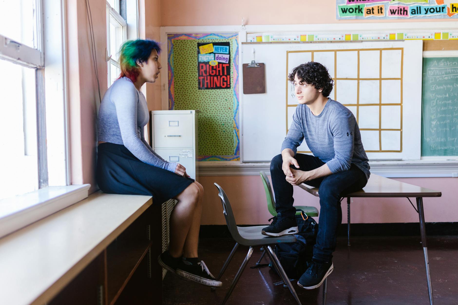 Two teenagers sitting at a small table talking calmly with a school counselor to resolve a disagreement.