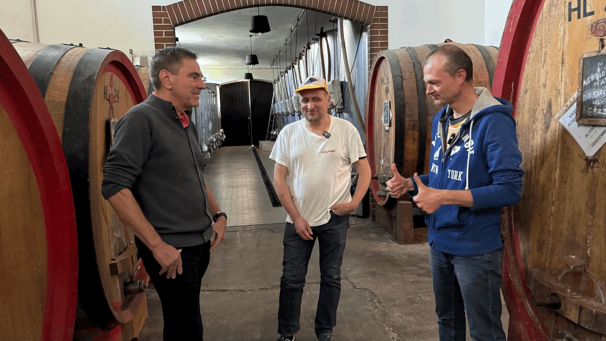 Pier Carlo and Gabriele discussing winemaking among large wooden barrels in the Giuseppe Cortese cellar.