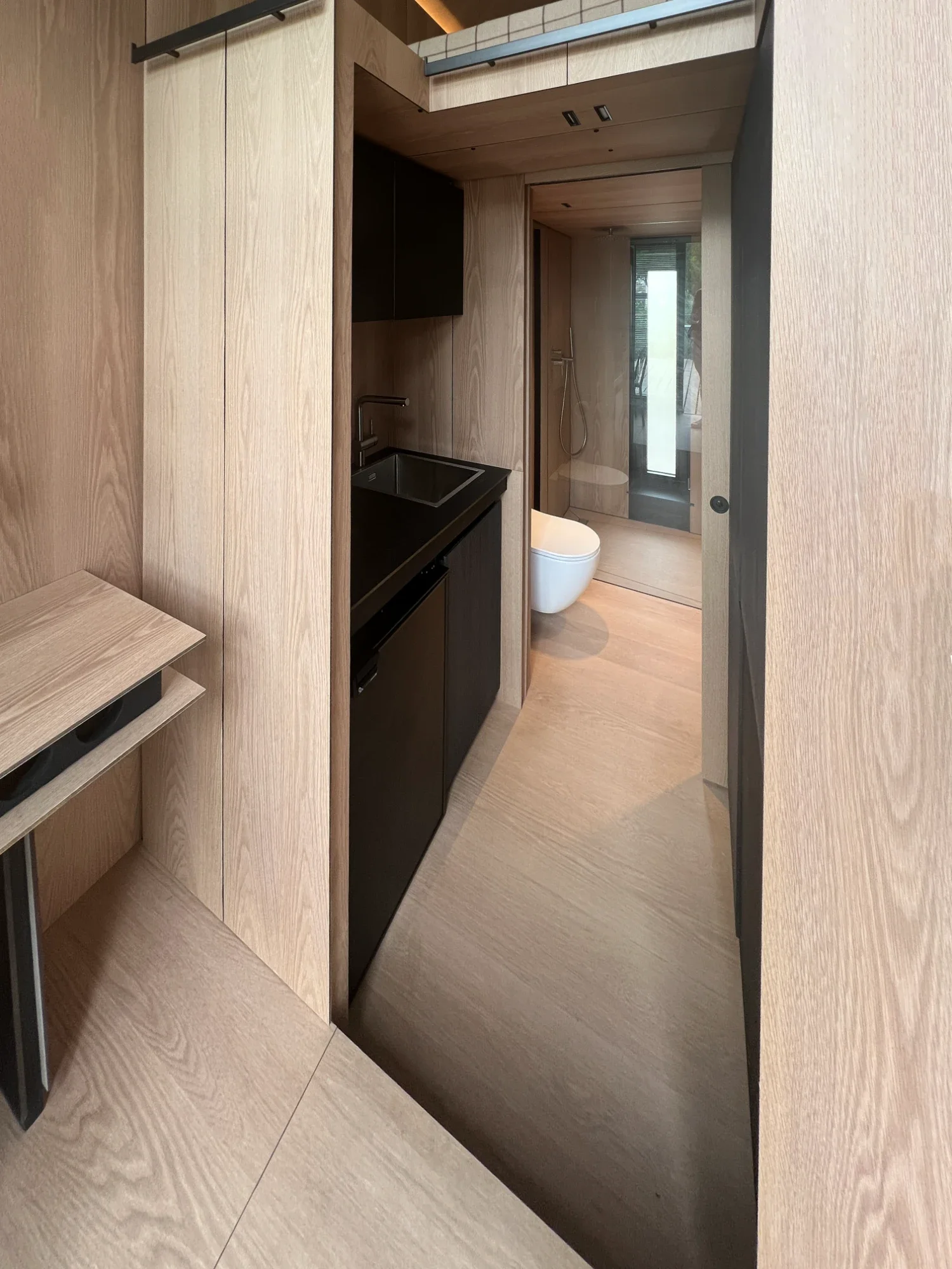 Intérieur de l'écolodge Villa Médicis, kitchenette noire et salle d'eau en enfilade, parquet chêne