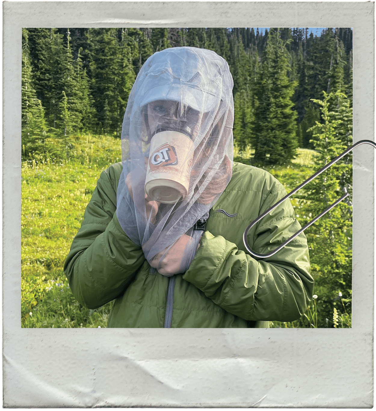 a polaroid picture of a woman drinking tea in the wildreness with a bug net obscuring her face