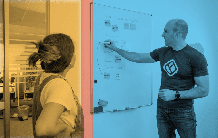 A woman in a pinstripe blazer works on a laptop while a man observes in a modern, brightly lit office setting.