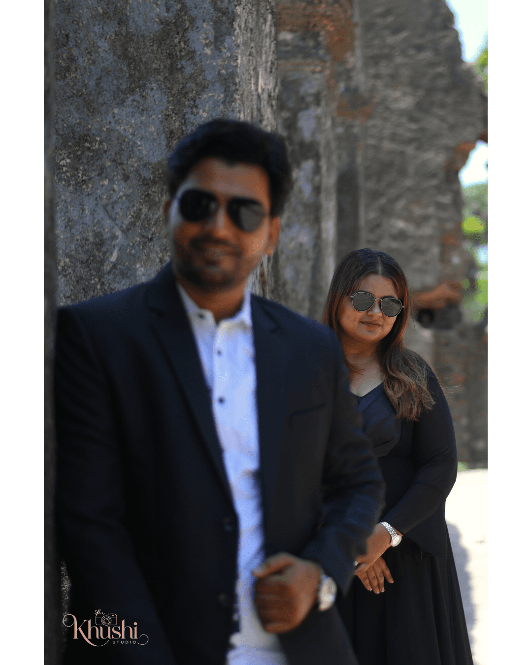 A couple stands hand-in-hand in front of a rustic stone building.