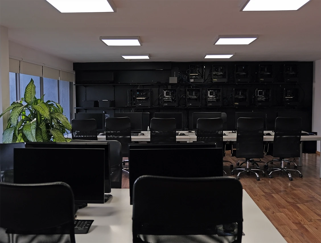 Modern workstation setup with multiple black chairs and computer monitors in a clean, minimalist office space.