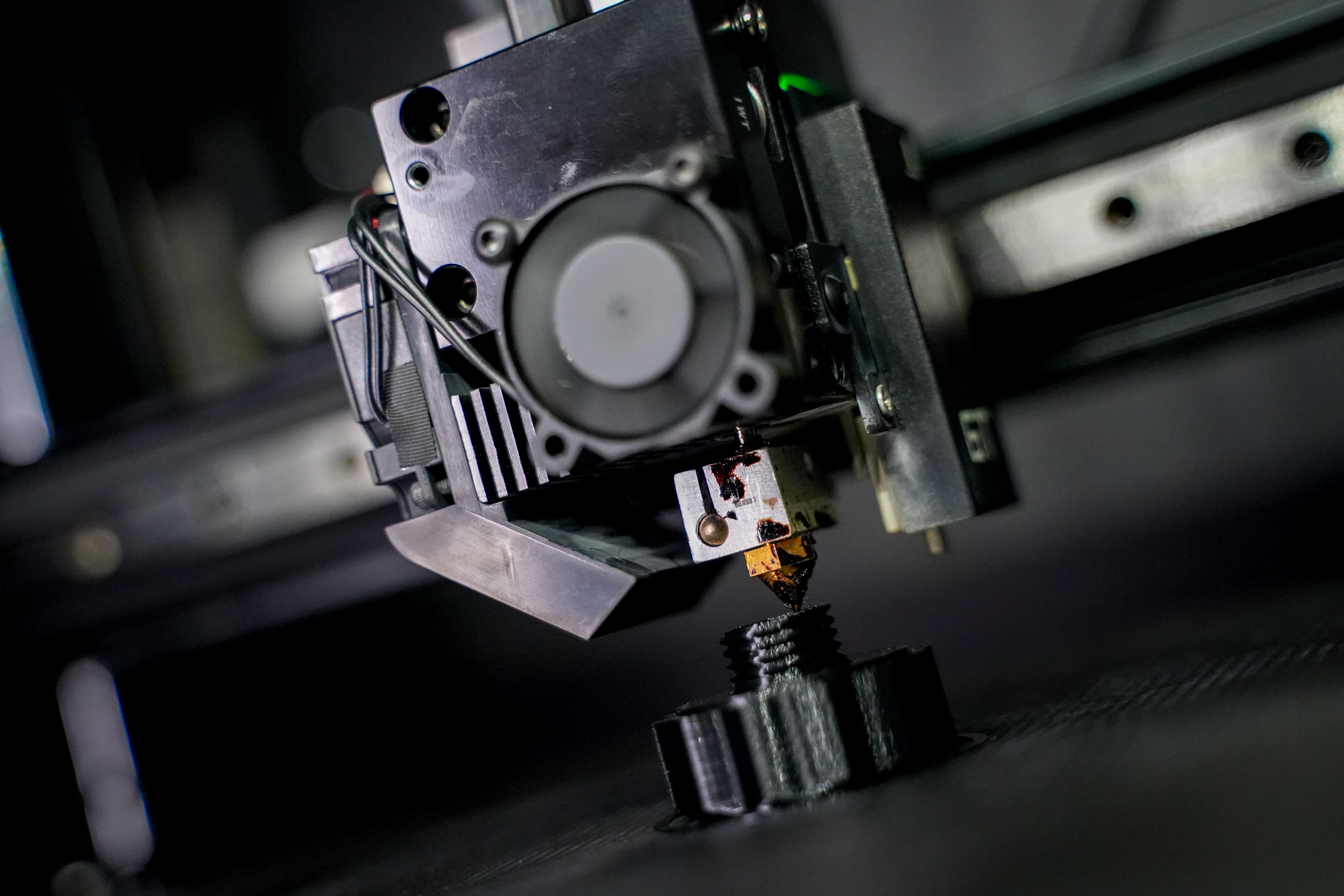 Close-up dell’hotend di una stampante 3D a filamento durante la stampa di un componente tecnico