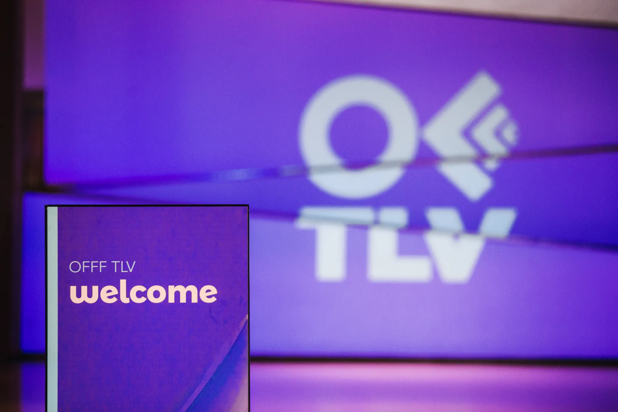 OFFF TLV festival venue with the OFFF logo projected on a purple wall beside a welcome screen