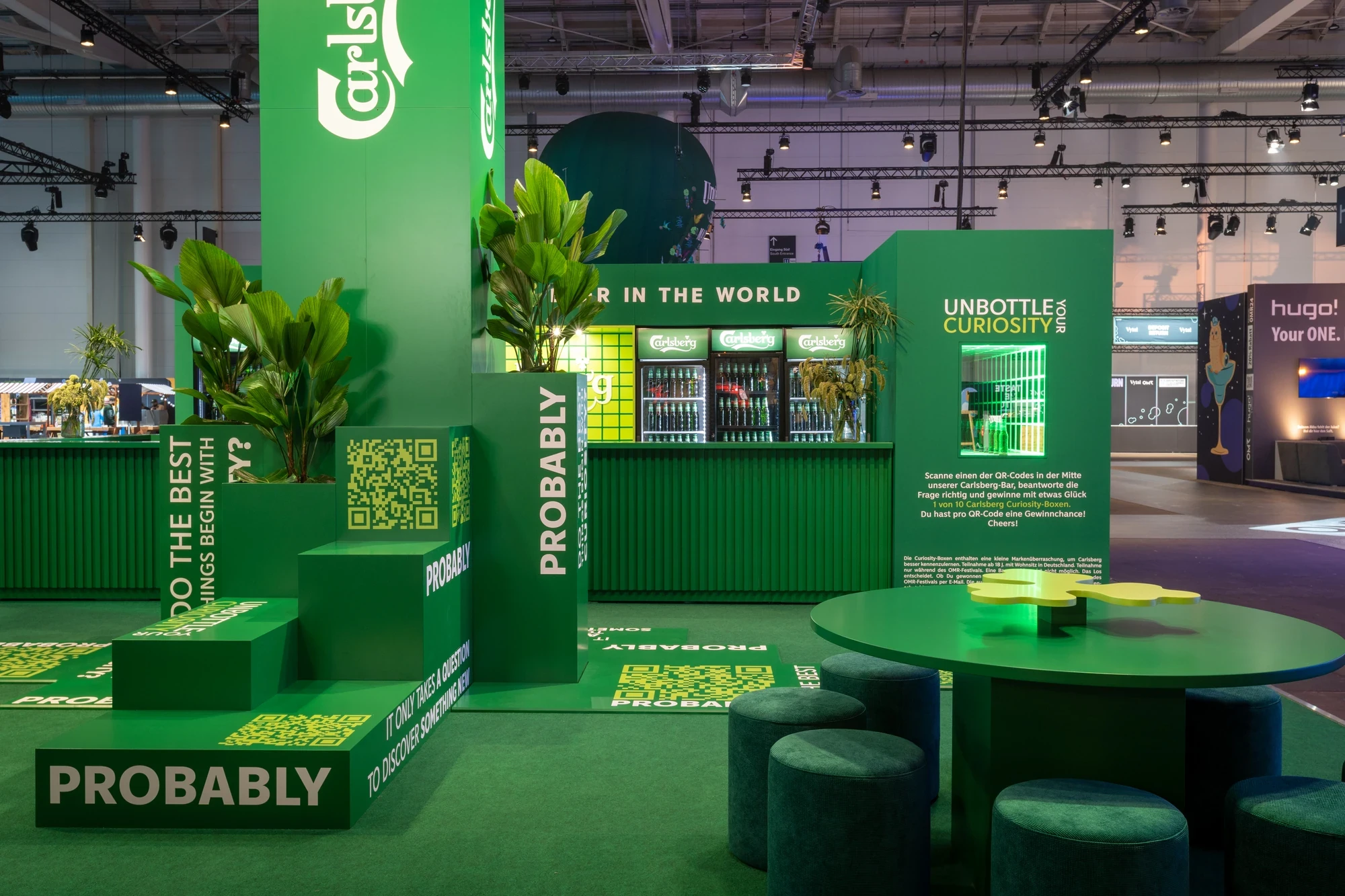 Carlsberg exhibition booth in vivid green with stacked „Probably" cube installations, branded fridges and the „Unbottle your Curiosity" wall.