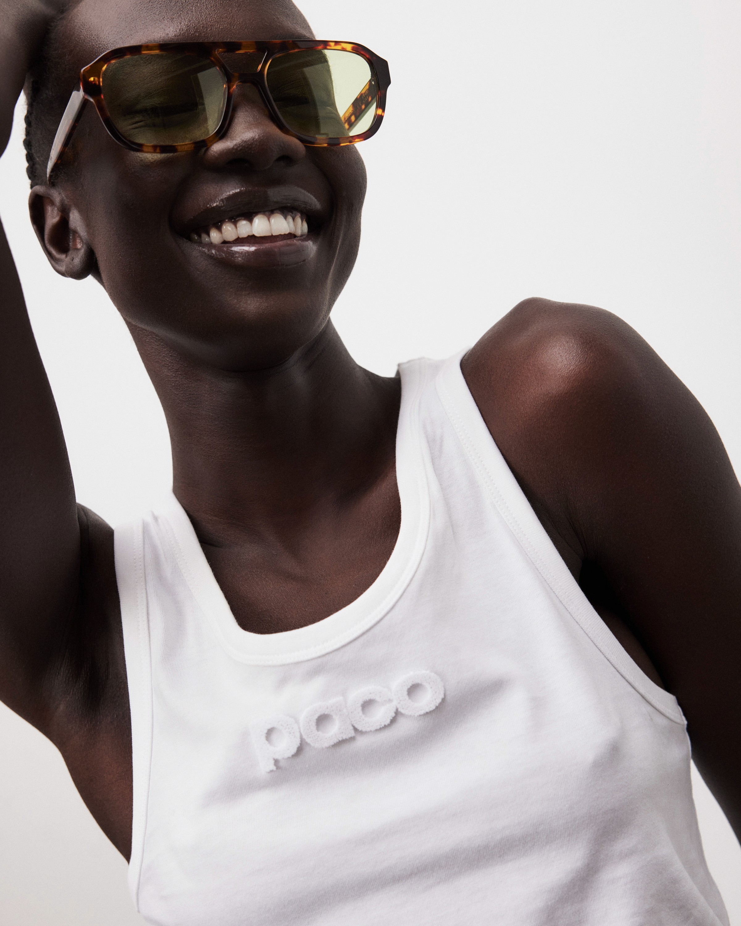 Fashion photography of a smiling model in a white singlet and large clear glassses.
