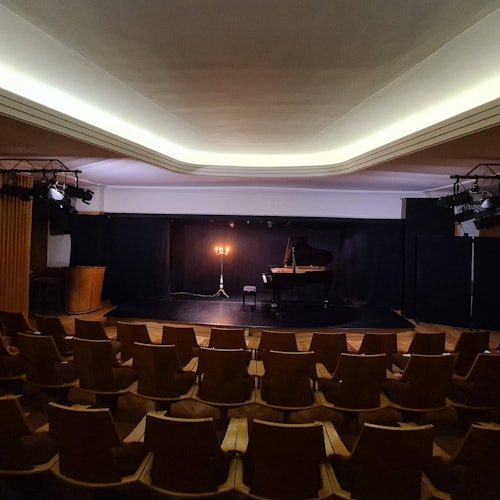 The photo shows the audience and the stage with the piano