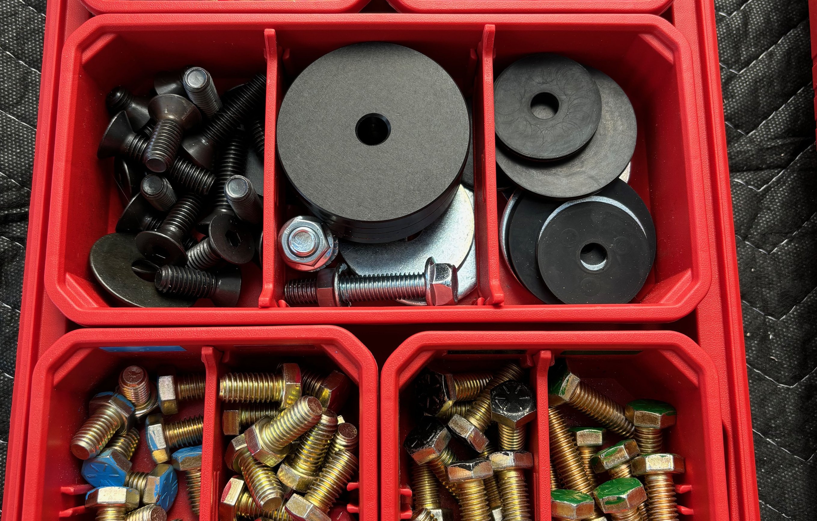 Red Milwaukee Packout organizer stocked with an assortment of bolts, washers, springs, and ball leveling head plates