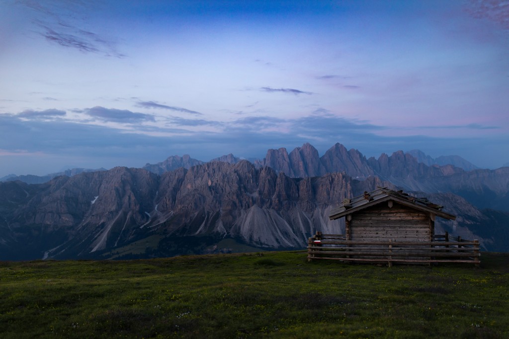 A small house on a grassy hill with mountains in the distance