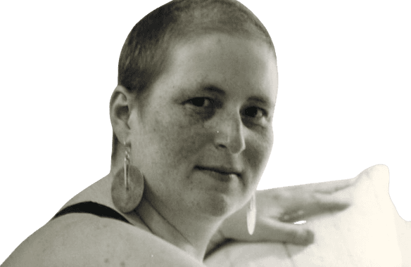 Black and white portrait of a woman with a shaved head, looking calmly at the camera with a slight smile. She wears large, round earrings and appears relaxed, exuding confidence and individuality. The simple background keeps the focus on her expressive face and distinctive style.