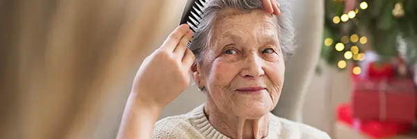 Elderly woman having her hair combed by caregiver