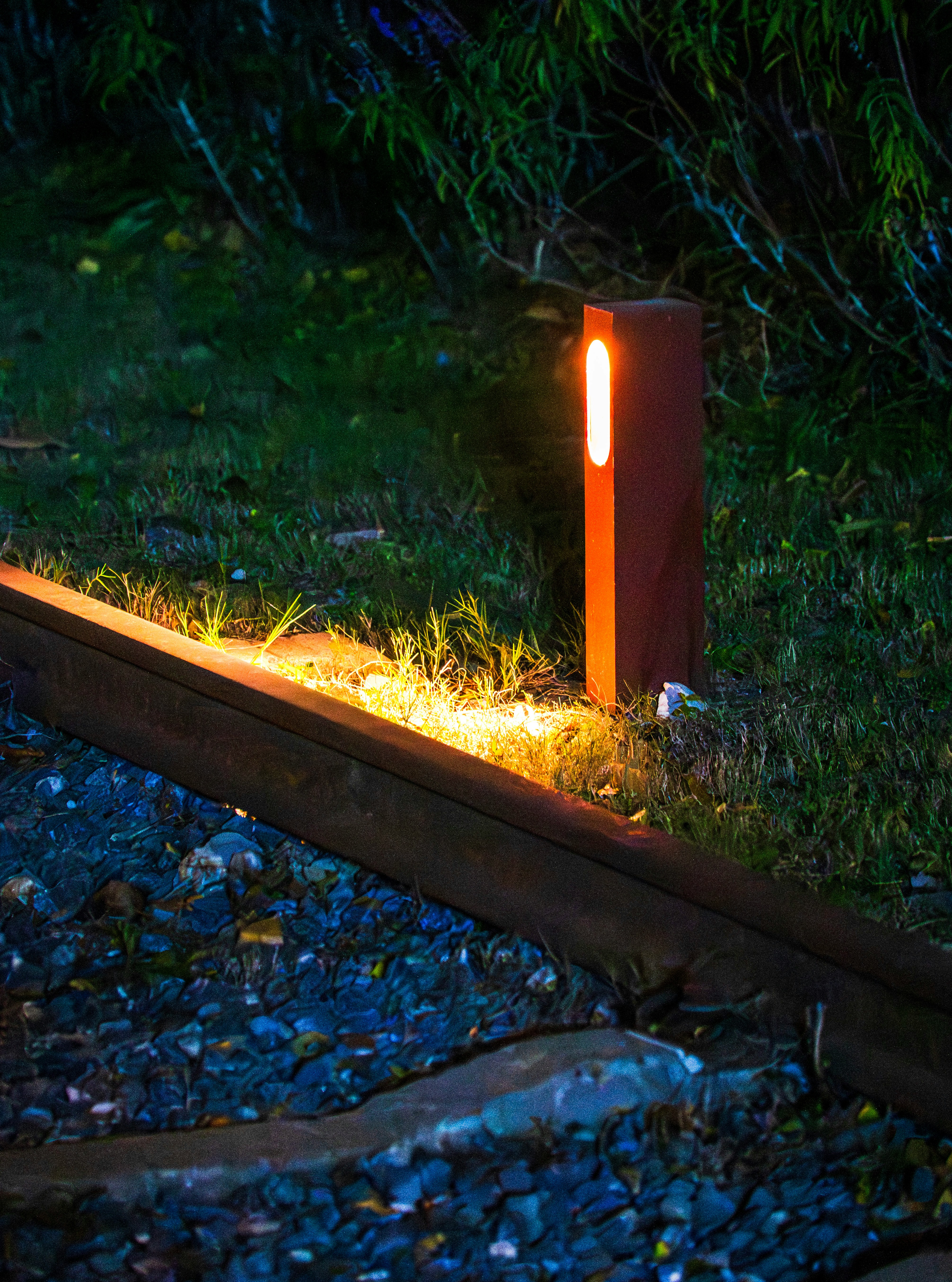 A single garden light illuminates train tracks at night.