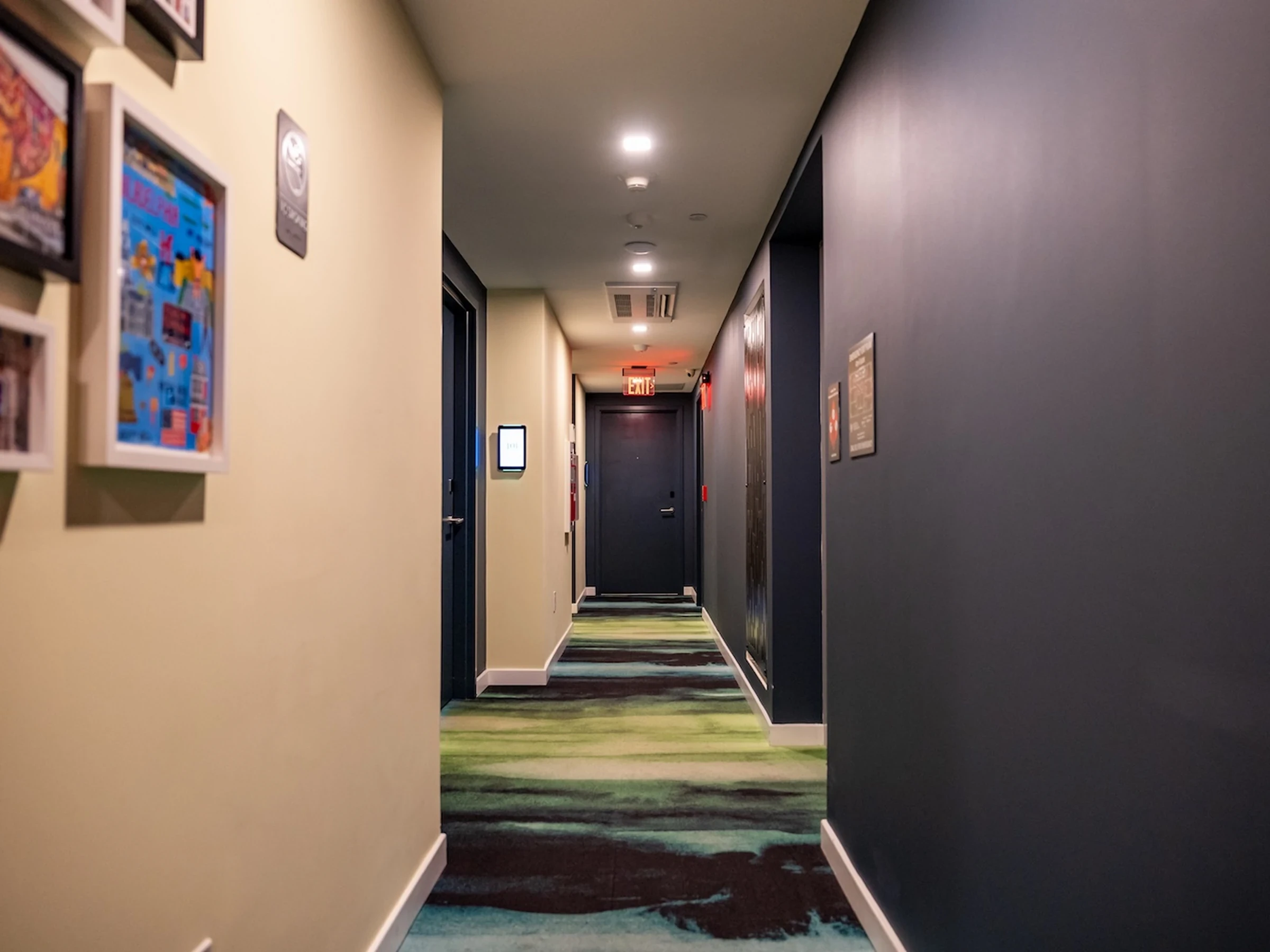 Patterned carpet tile flooring in a boutique hotel hallway corridor with colorful wall art and recessed lighting.