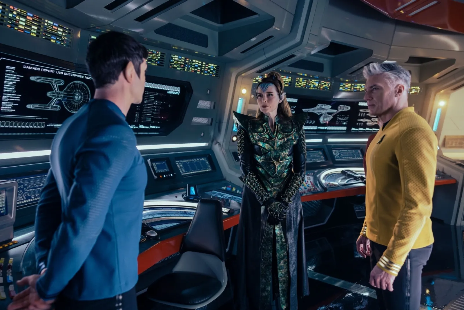 Three individuals in futuristic uniforms are standing in a high-tech spaceship control room, featuring multiple display screens and advanced control panels.