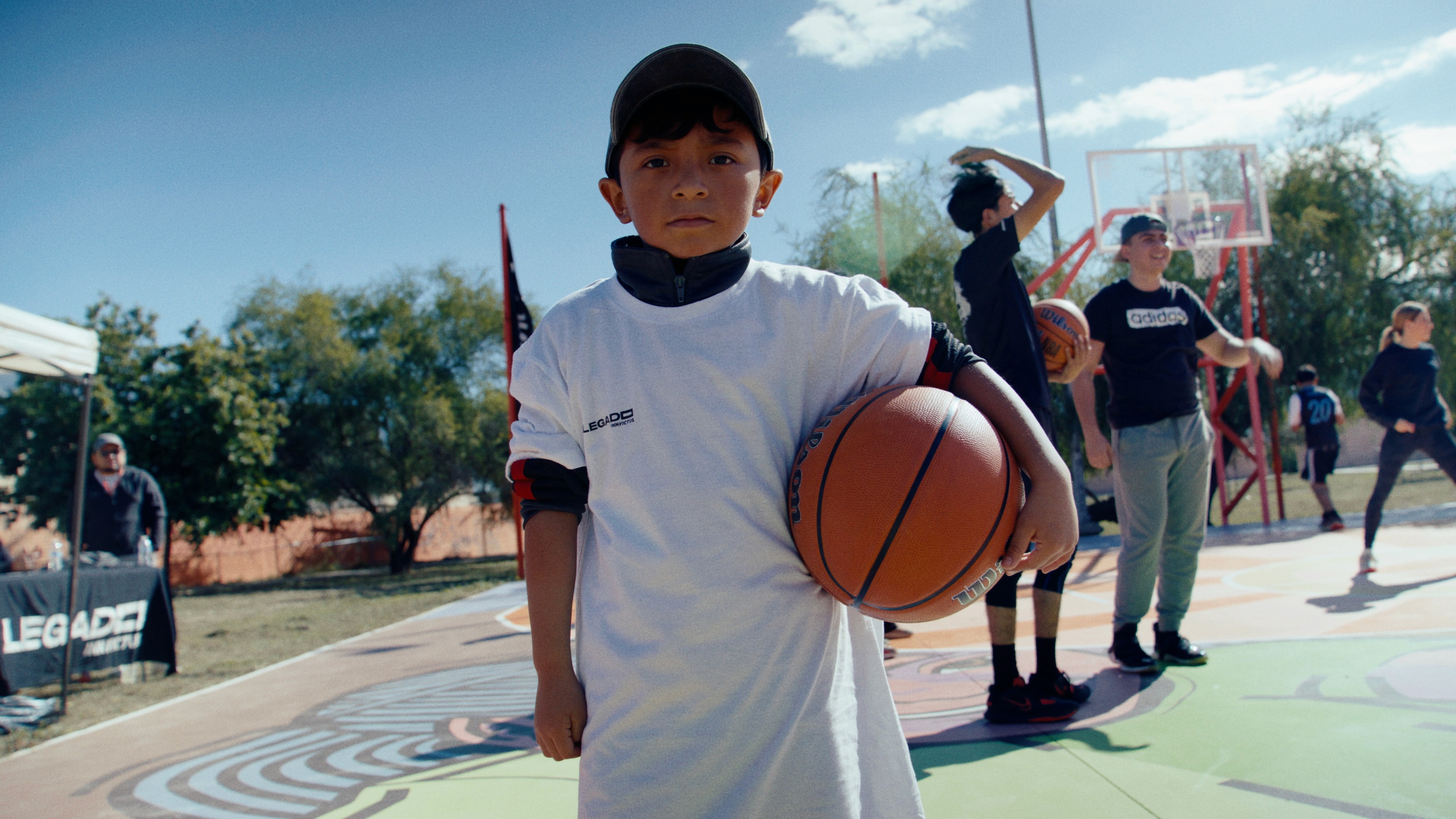 Close-up portrait of a person wearing a gray insulated hooded jacket with the hood up, showing their face framed by the hood against a light background.