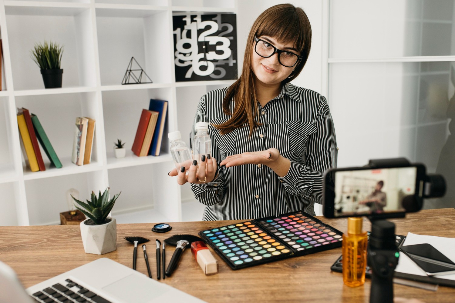 A woman holds a makeup bottle in one hand and a camera in the other, showcasing her passion for beauty and photography.