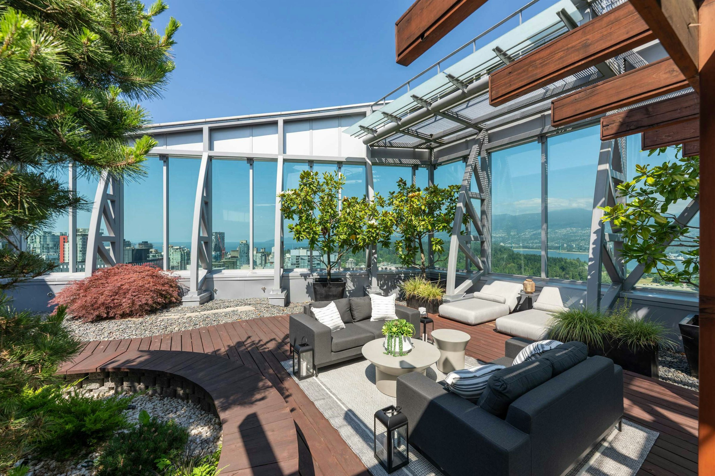 Rooftop terrace with modern furniture, greenery, and panoramic views of the city skyline under a bright blue sky.