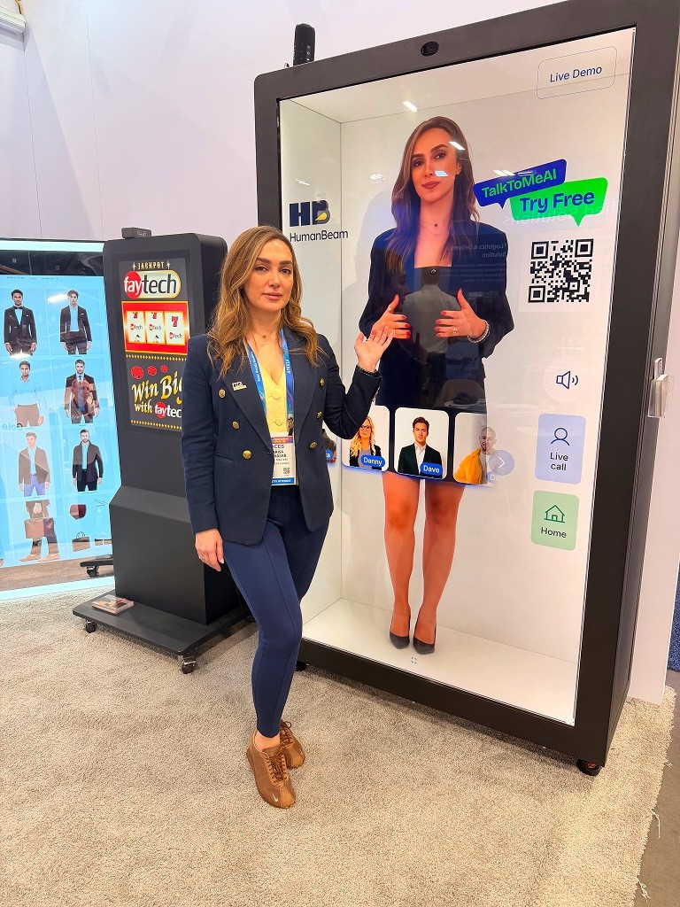 A presenter standing next to a large HumanBeam holographic display at the booth during CES 2026, showcasing a life-sized AI avatar for immersive customer service.