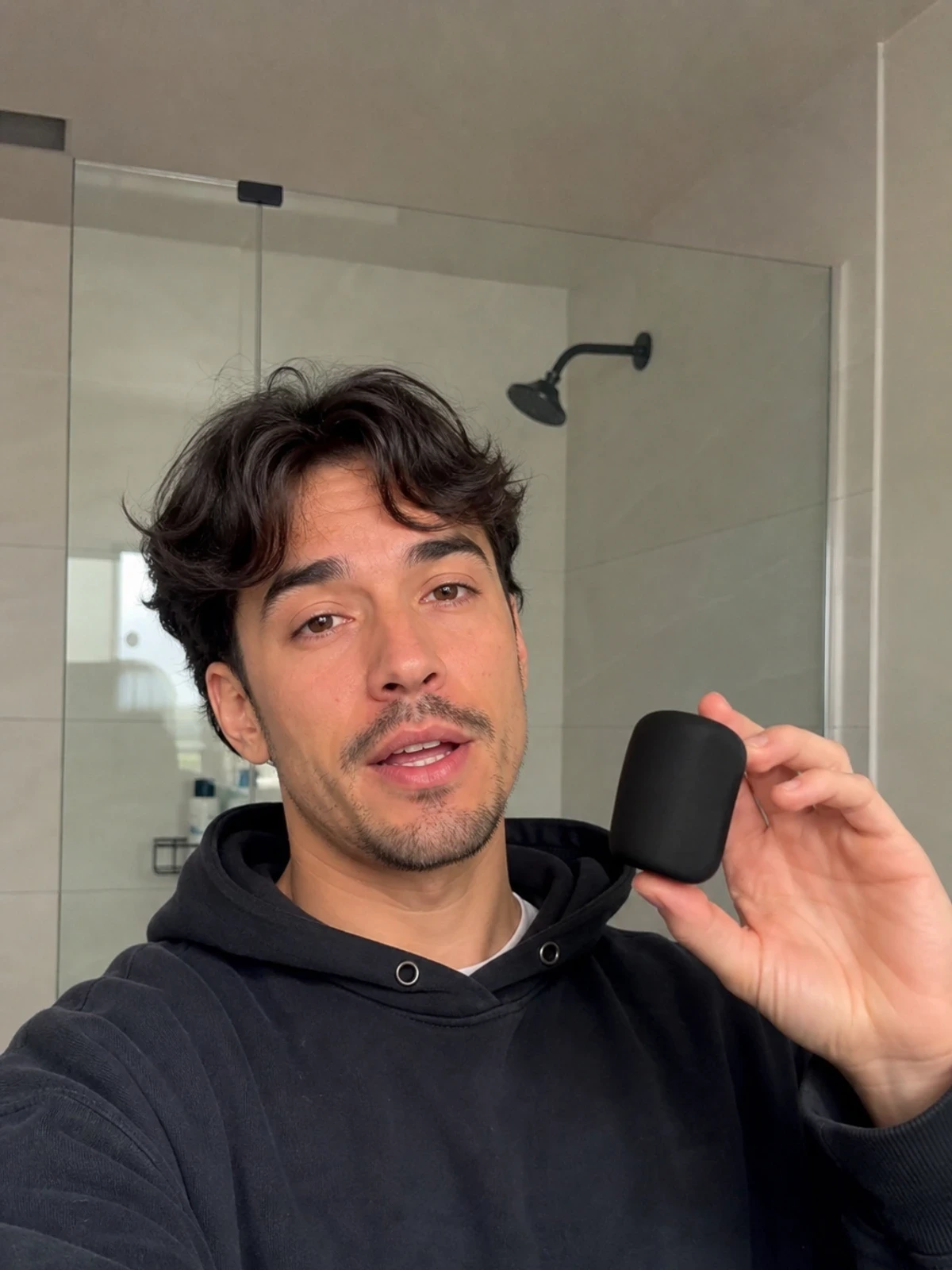 UGC-style photo: streetwear creator, in a bathroom mirror setup, demonstrating a simple hand-sized product while talking to camera, casual handheld angle.