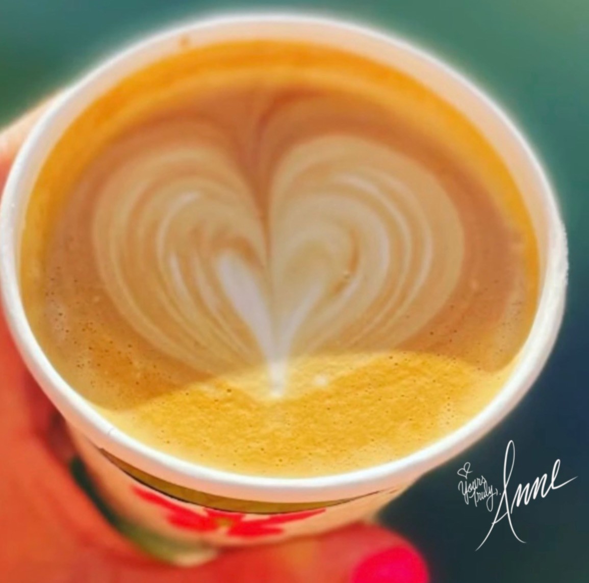 Hand holding a cup of coffee with heart-shaped foam